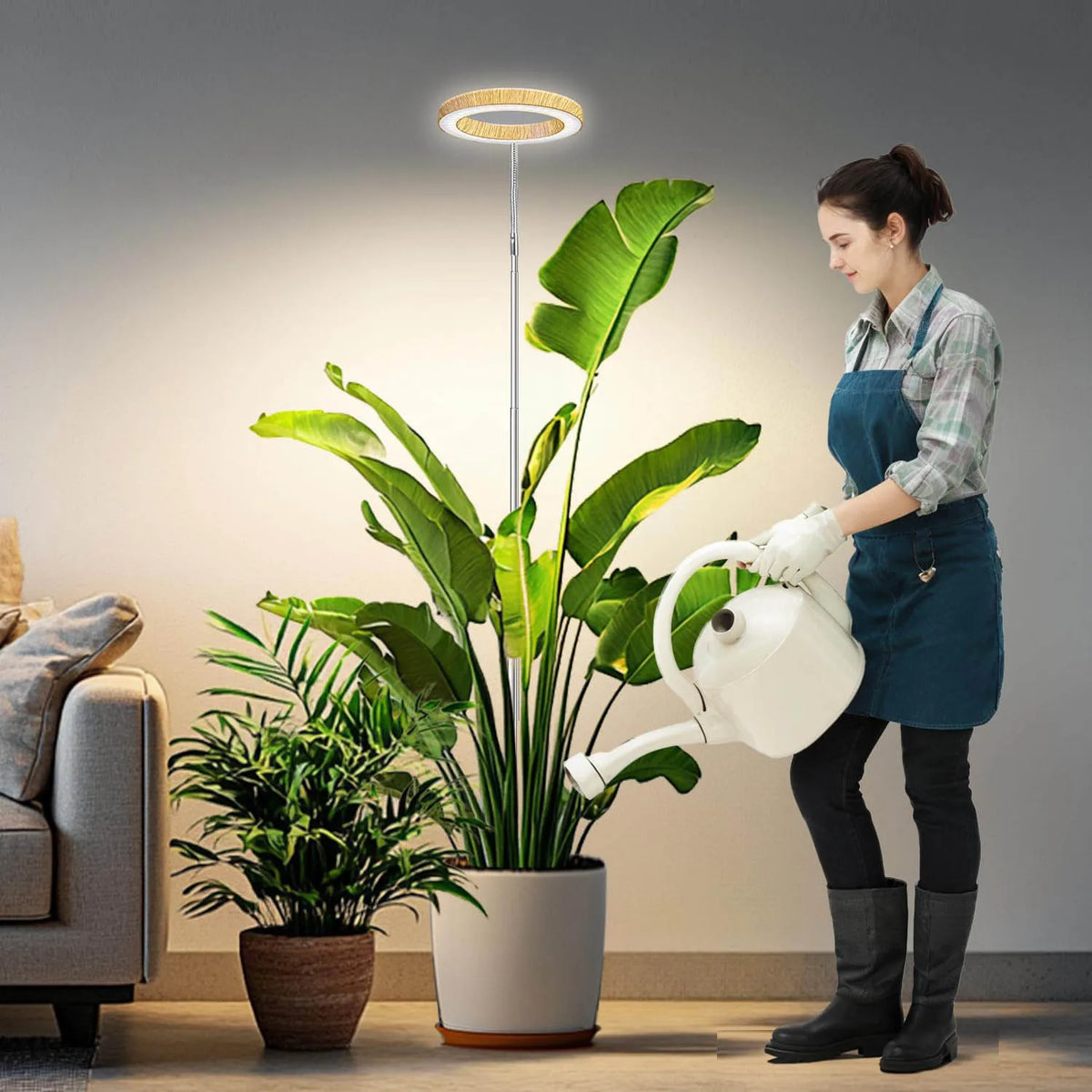 A woman is using a white watering can to water a large green plant in a pot next to a modern LED grow light.