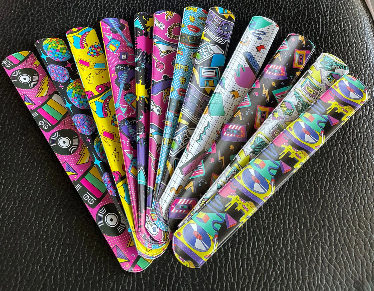 A collection of twelve colorful retro 80s and 90s slap bracelets arranged diagonally on a dark surface.