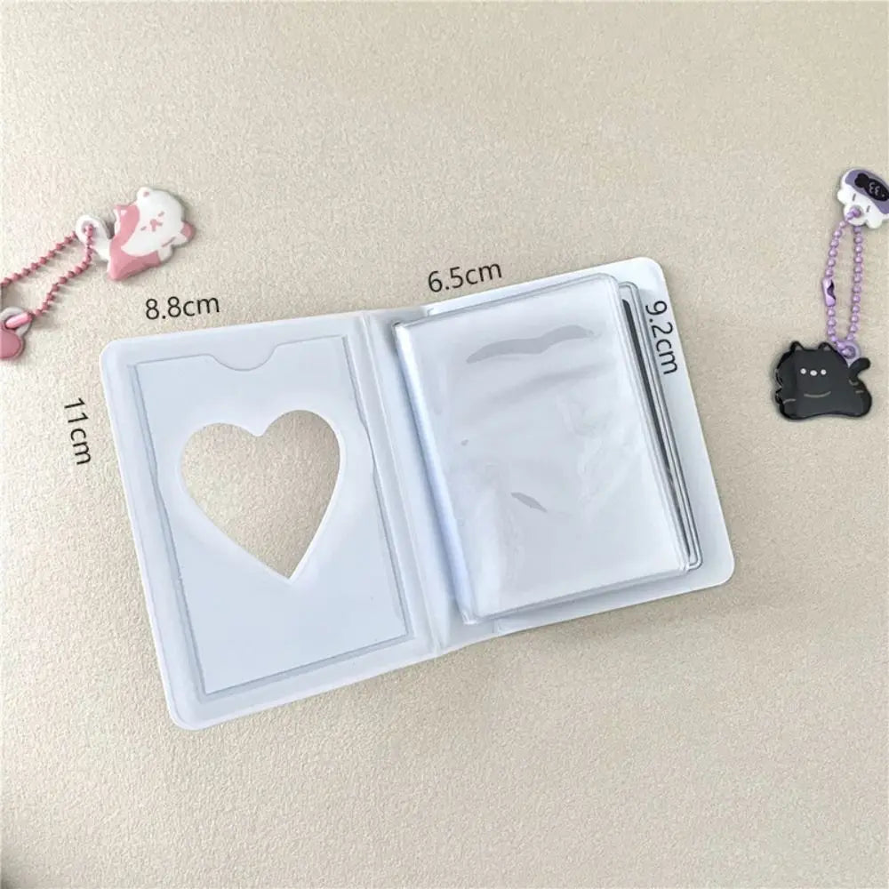 A clear photo album with a heart cutout and a lid, next to small pink and black bear charms.