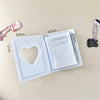 A clear photo album with a heart cutout and a lid, next to small pink and black bear charms.