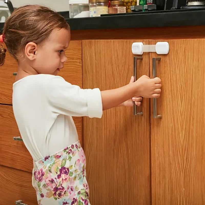A young girl is operating a child safety cabinet lock with a flexible strap on a wooden cabinet door.