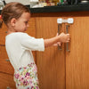 A young girl is operating a child safety cabinet lock with a flexible strap on a wooden cabinet door.