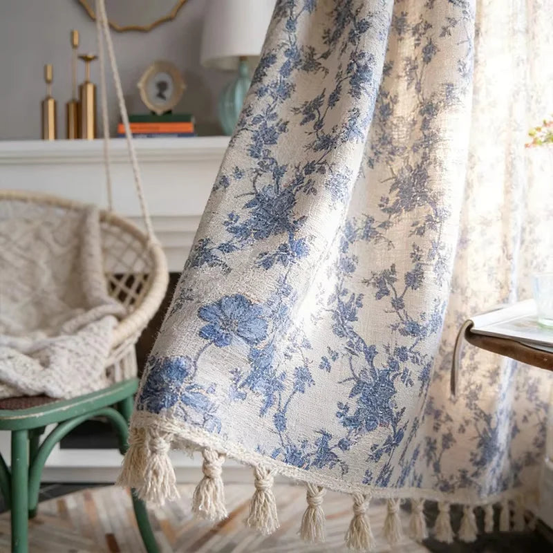 A light blue floral cotton-linen curtain with tassels hanging in a bright interior setting.