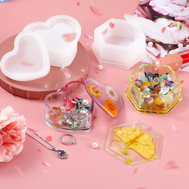 A set of silicone jewelry boxes and resin molds in pink and clear colors displayed on a pink background.