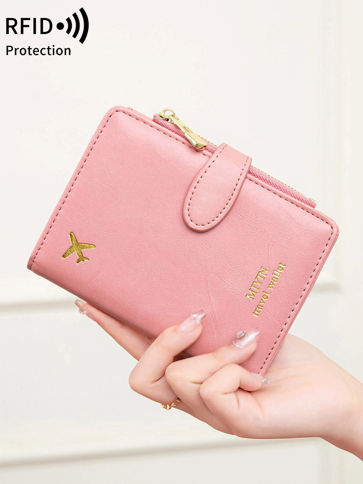 A pink leather passport wallet with an airplane pattern and RFID protection is being held by a hand.