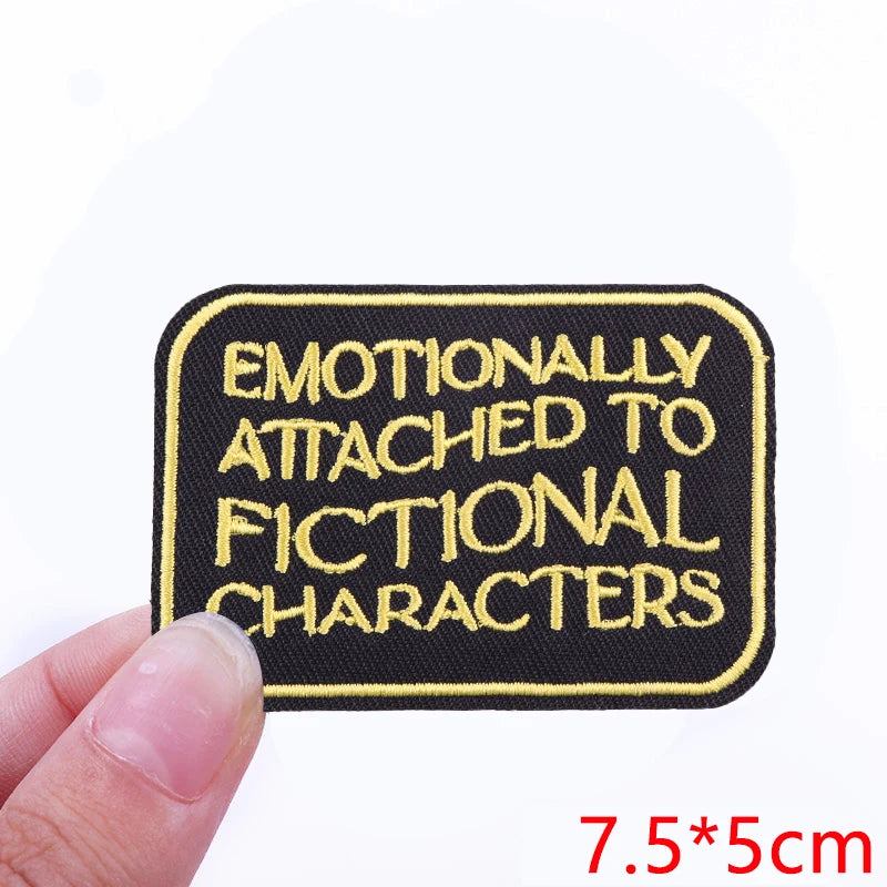 Black embroidered iron-on patch with yellow text that reads Emotionally Attached to Fictional Characters
