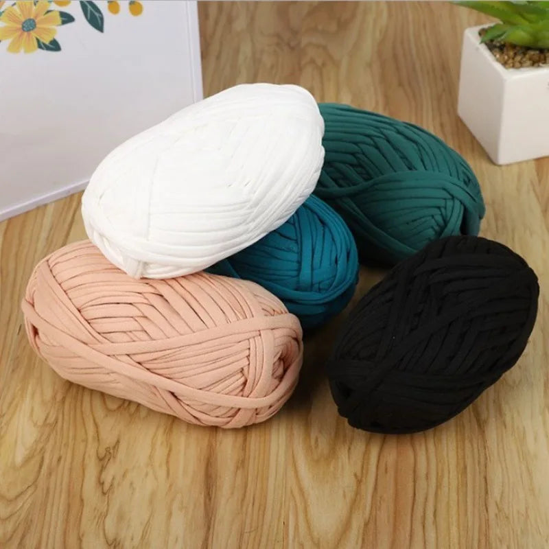 A collection of various colored soft T-shirt yarn skeins including white, teal, pink, and black lying on a wooden surface.