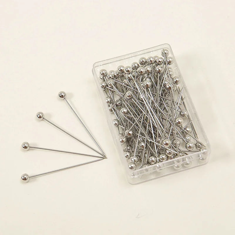 A clear plastic container holds a pack of 100 silver precision quilting pins for sewing and crafting.