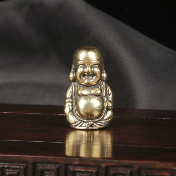 Vintage brass Maitreya Buddha desk ornament with a smiling face resting on a dark wooden surface.