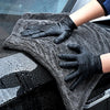 Hände in schwarzen Handschuhen reinigen ein Auto-Fenster mit einem grauen Mikrofasertuch.