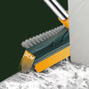 A close-up of a green and yellow rotating floor scrub brush with a long metal handle resting on a white surface.