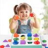 A smiling toddler holds red geometric shapes above a green wooden sorting box filled with various colored wooden shapes.