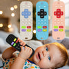 A baby is holding a black silicone teething remote toy next to three colorful silicone versions.