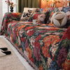 A richly colored floral jacquard sofa blanket with tassels draped over a bed.