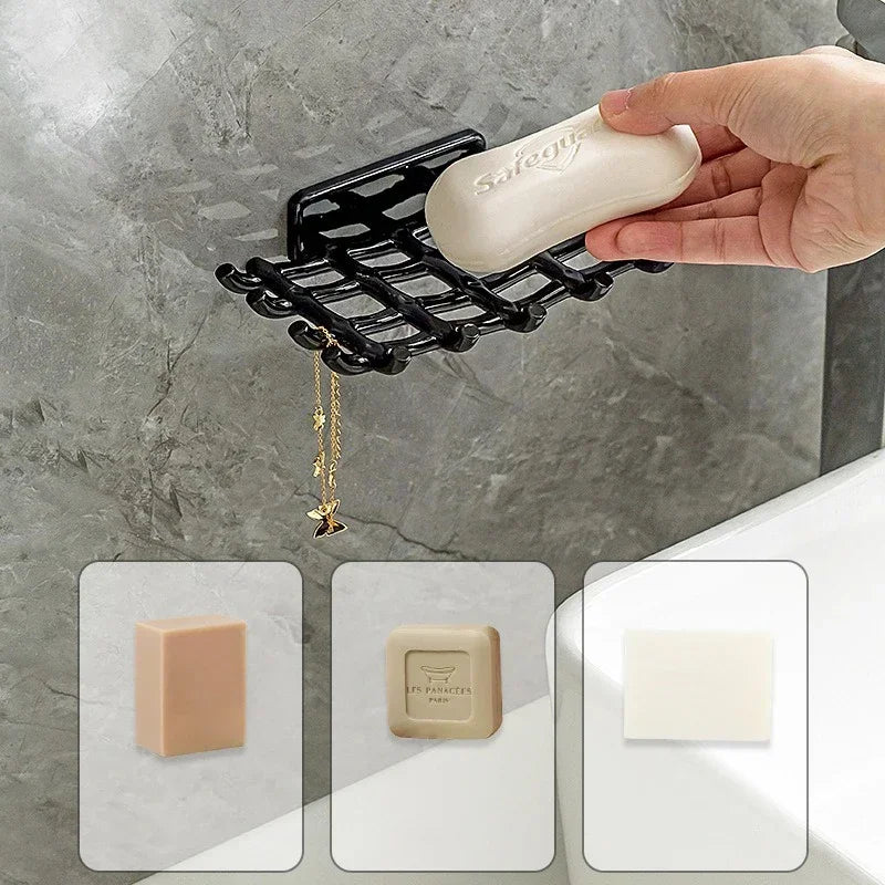 A hand holds a light beige soap bar over a black wall-mounted soap dish with a gold chain.