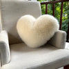 A light beige upholstered armchair features a fluffy white heart-shaped throw pillow.