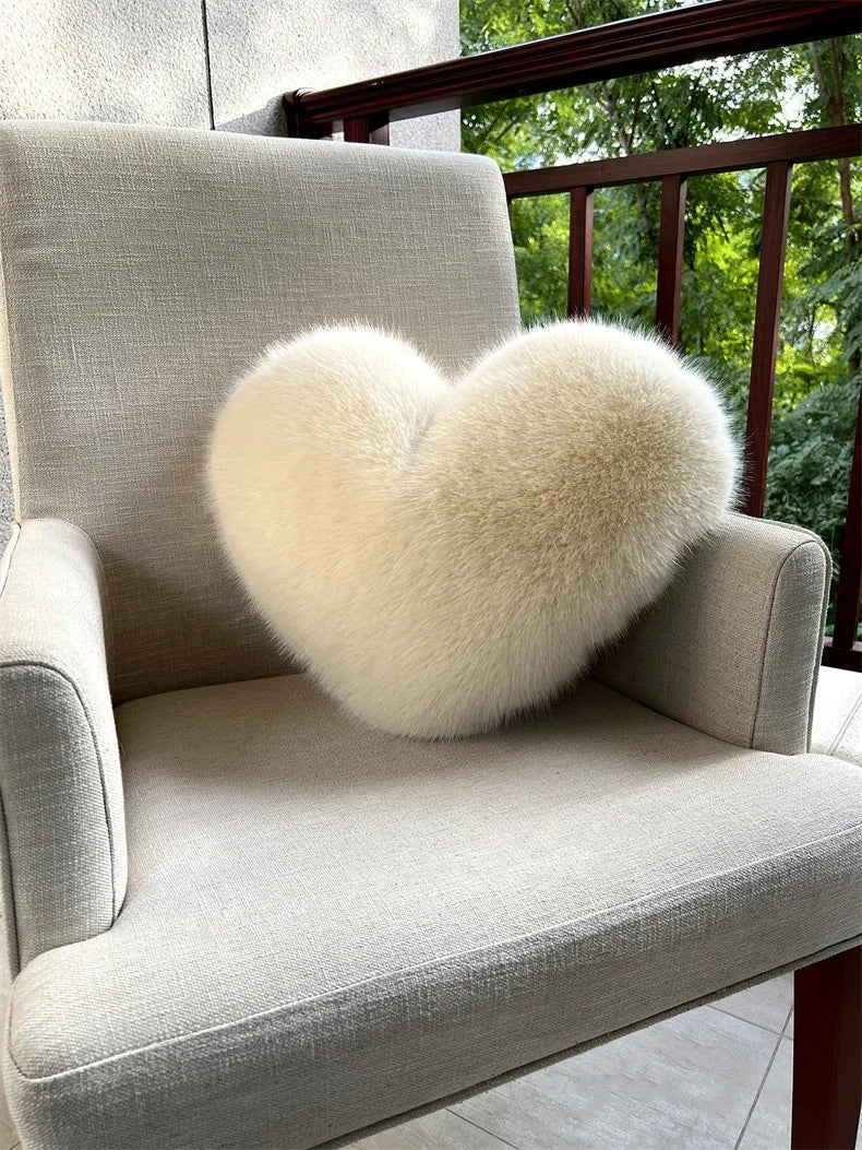 A light beige upholstered armchair features a fluffy white heart-shaped throw pillow.
