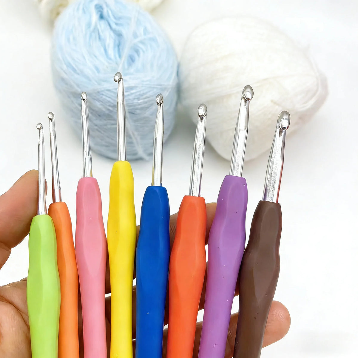 A hand holds an 8-piece crochet hook set with various colored ergonomic knitting needles.
