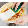 A hand is using a green scouring pad on a white plate stained with orange food residue.