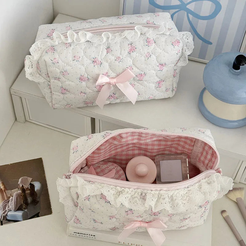 A white cosmetic pouch with pink rose print and lace trim is displayed on a white surface.