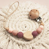 A wooden pacifier clip with crochet beads and a chain rests on a cream-colored knitted surface.
