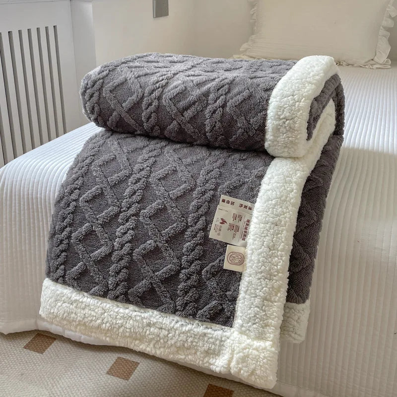 A gray double-layer fleece throw blanket folded on a white bed with a white striped cover.