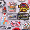 A collection of embroidered iron-on patches featuring various phrases and designs like book lover Satan loves me and see the 