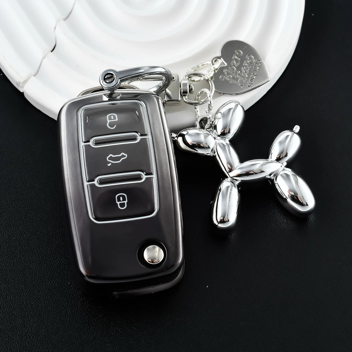 A silver car key fob attached to a keychain charm resting on a white car key cover.