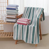 A striped bath towel set featuring teal and white stripes, with a pink folded towel resting on the fabric.