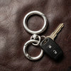 Silver snap hooks and a key attached to a keyring resting on brown leather.