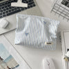 A light blue and white striped makeup bag with a floral embroidery detail resting on a desk next to a laptop and mouse.