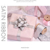 A pink gift box tied with a silver satin ribbon and a roll of matching satin ribbon.