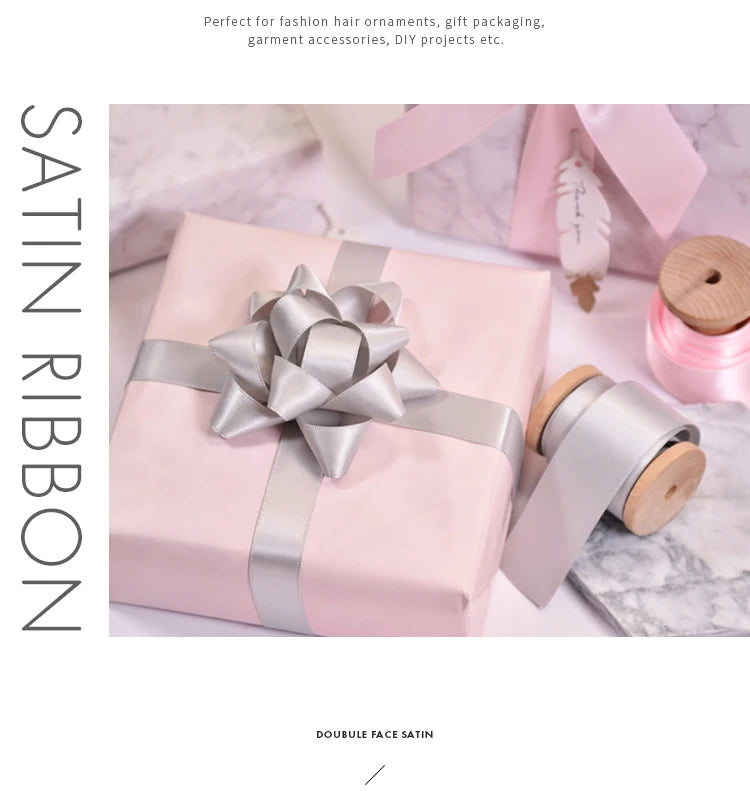 A pink gift box tied with a silver satin ribbon and a roll of matching satin ribbon.