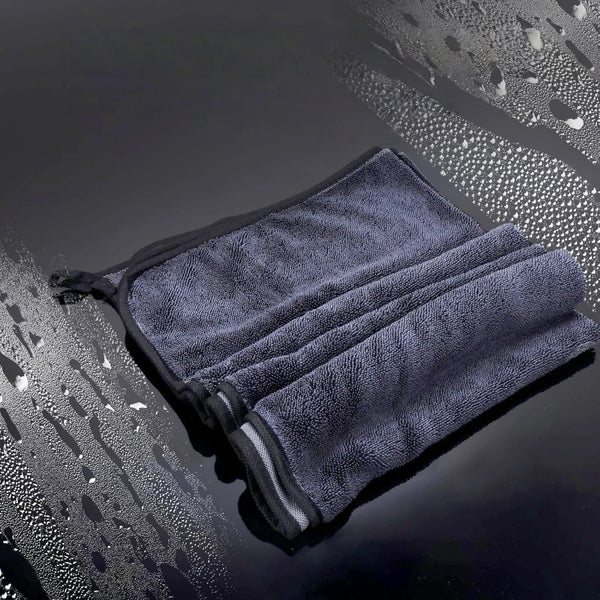 A stack of dark gray microfiber drying towels is shown on a wet, reflective surface.