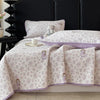 A light purple and white floral quilted bedspread is displayed on a dark headboard.