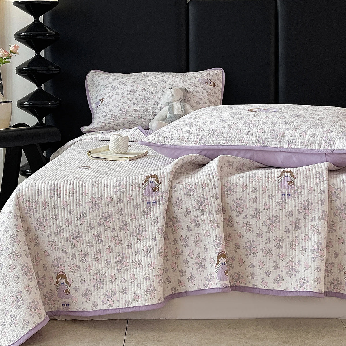 A light purple and white floral quilted bedspread is displayed on a dark headboard.