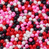 A close-up of small round imitation pearl beads in various shades of pink, red, white, and black.
