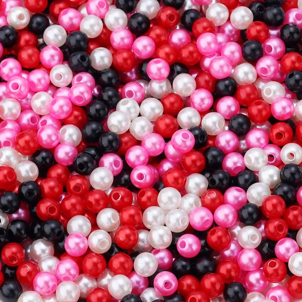 A close-up of small round imitation pearl beads in various shades of pink, red, white, and black.
