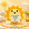 Handmade crochet sun-themed pocket hug doll in bright yellow orange yarn sitting on a woven mat.