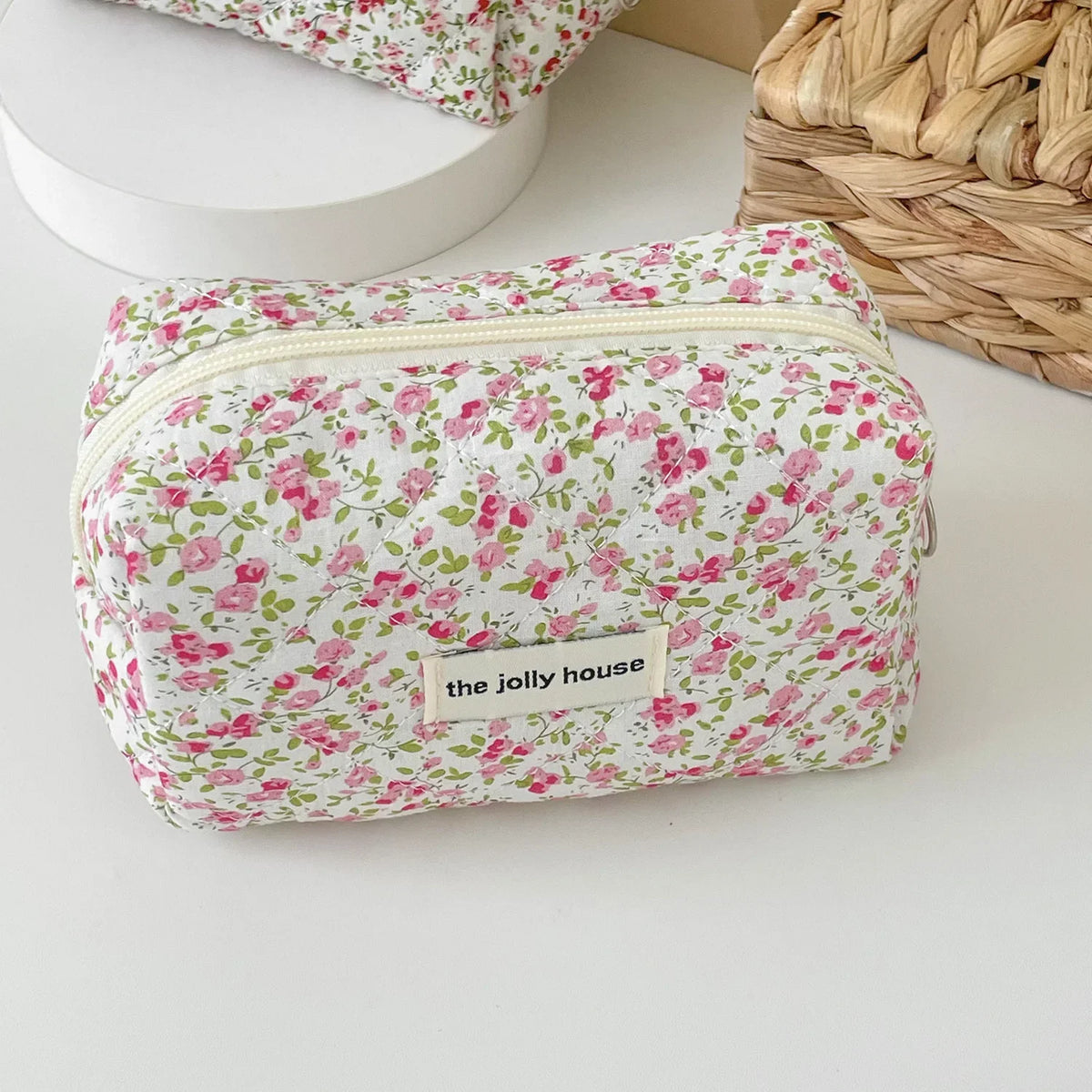 A pink floral quilted makeup bag with a zipper closure resting on a white surface.