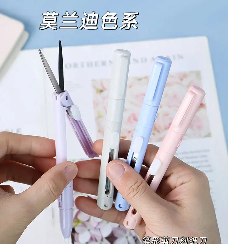 A hand holds several folding pen-shaped safety scissors in various colors, including purple, white, blue, and pink.