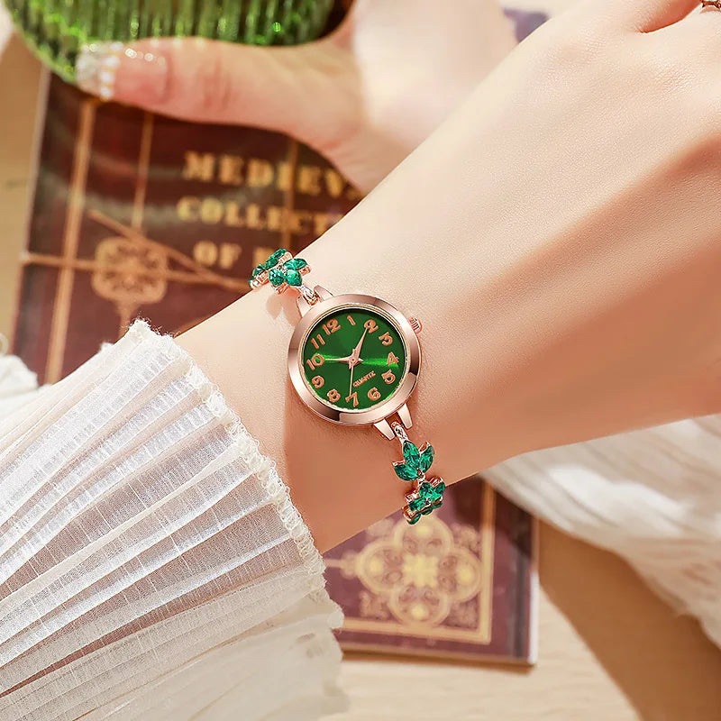 Nahaufnahme einer eleganten Strassarmbanduhr mit grünem Zifferblatt und pinkem Metallarmband, getragen am Handgelenk.