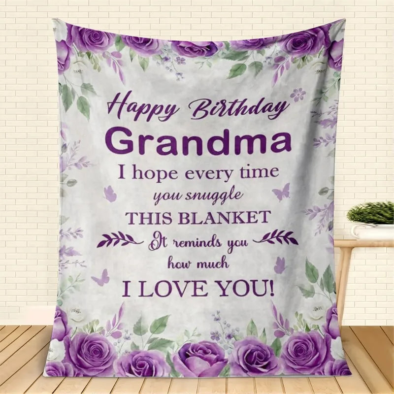 Lila Blumendecke mit 'Alles Gute zur Geburt Oma' und Rosen als Geschenk.