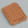 A stack of brown PU leather sewing labels with the text Handmade with Love stamped on them.