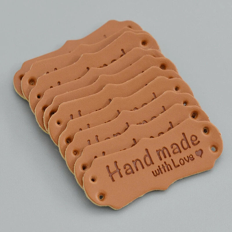 A stack of brown PU leather sewing labels with the text Handmade with Love stamped on them.