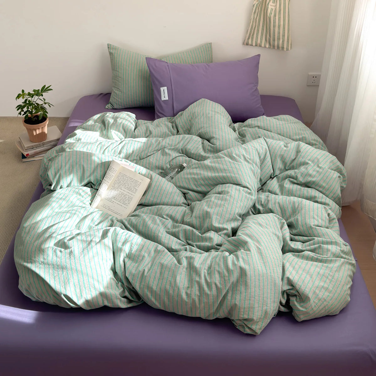 A light green and white striped duvet cover set displayed on a purple bed with lilac pillows.