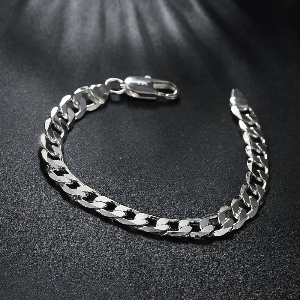 A silver chain bracelet with a clasp is displayed on a dark surface.