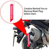 A close-up of a rubber exhaust wash plug with a keychain tag being removed from a motorcycle's exhaust system.