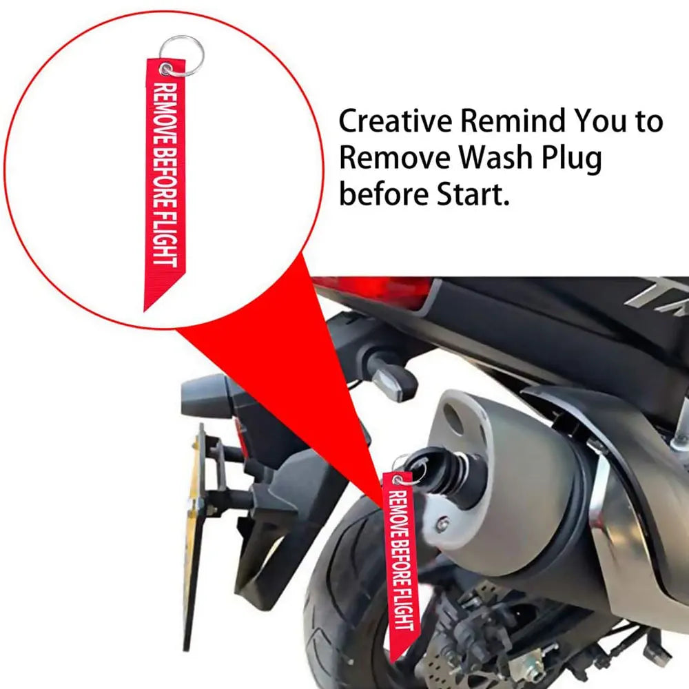 A close-up of a rubber exhaust wash plug with a keychain tag being removed from a motorcycle's exhaust system.