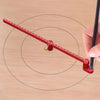 A red aluminum circle drawing ruler is being used to find the center of a circle on a wooden surface.